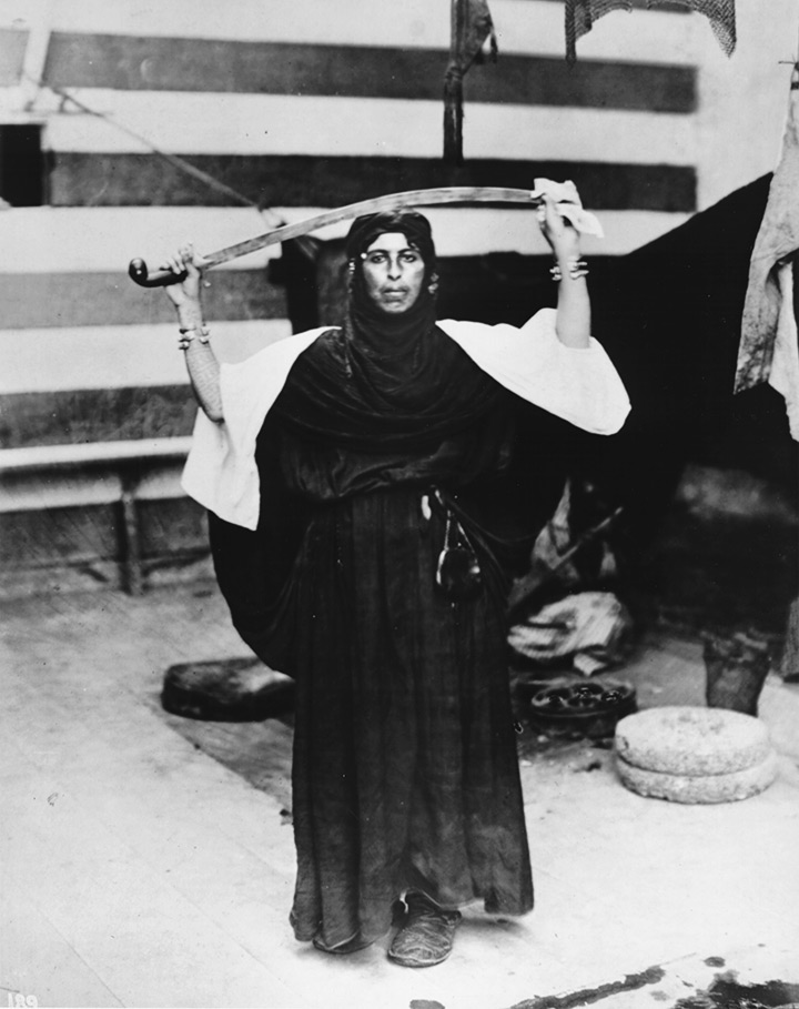 <h4>Photographed by Jesse Tarbox Beals</h4>
<p>A Bedouin woman, dressed in native costume, holds a scimitar above her head while performing a sword dance.</p>
