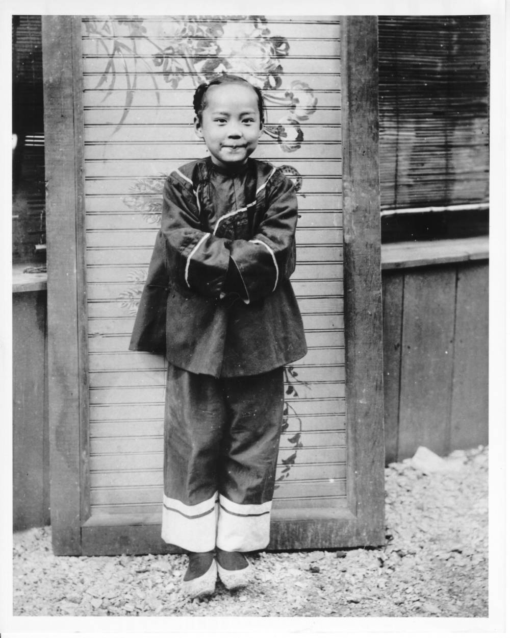 <p>Aro Moy, a young Chinese girl in traditional dress, poses in front of a building in the Chinese Village on the Pike. Chinese children played a role in the Chinese exhibits. Some would sing, while others would dance. Other children would play musical instruments.</p>
