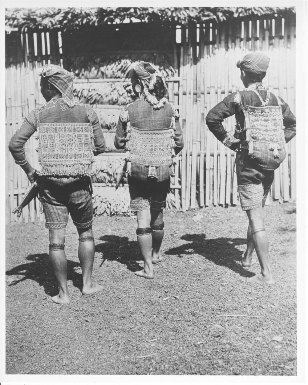 <p>Three Bagobo men in traditional dress turn their backs to the camera to show elaborately-beaded hunting bags.</p>
